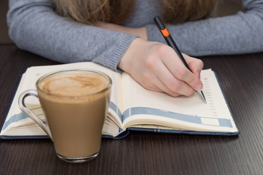 woman writing in planner drinking coffee