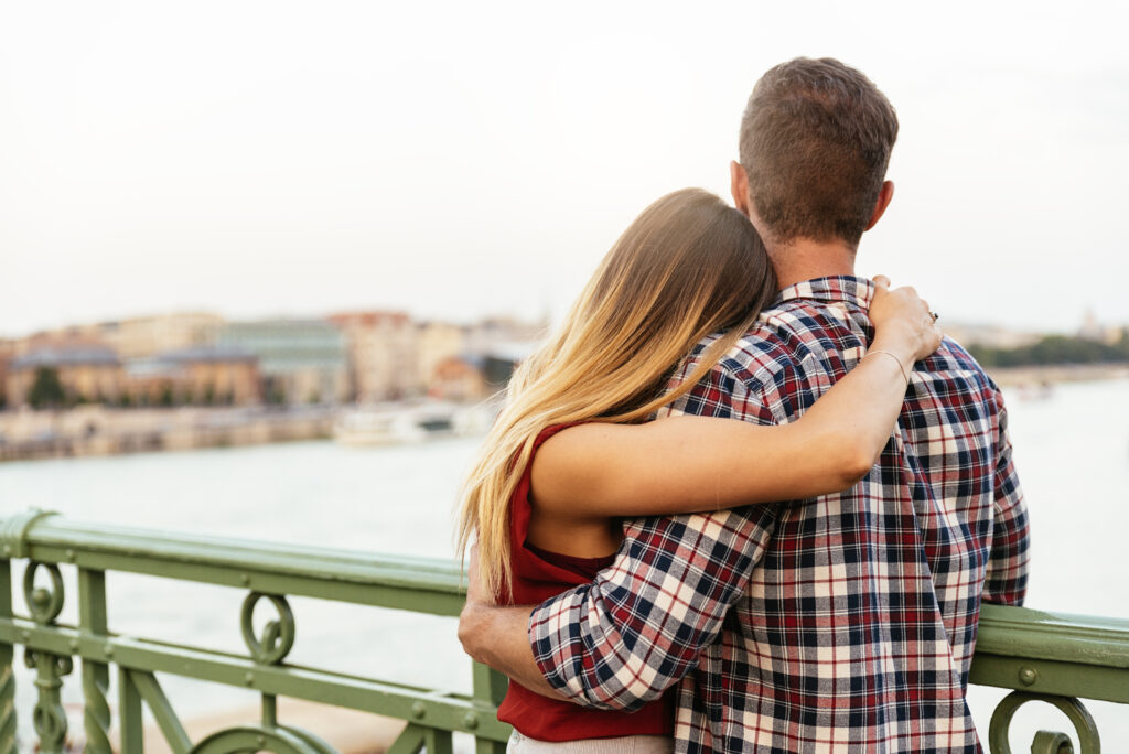 young couple hug each other while looking out at a river