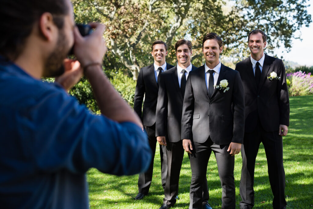 Photographer taking photo of groom and groomsmen at park