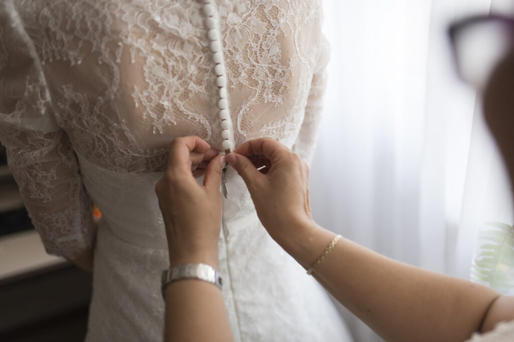Woman buttoning the bride's wedding dress