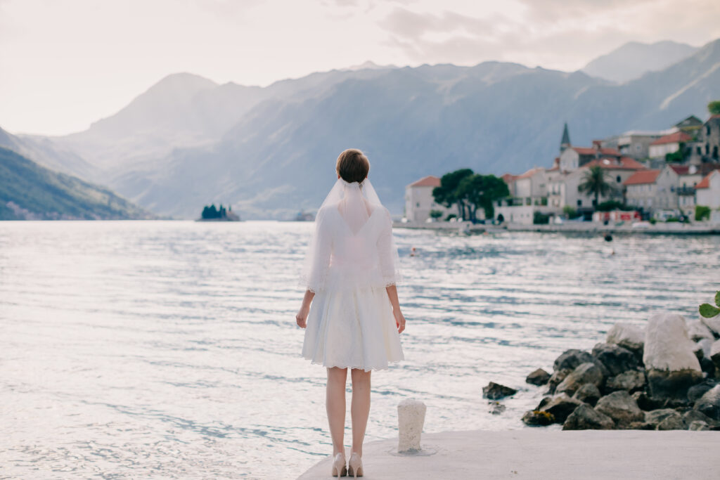 bride in a short wedding gown looks out at mountains and lake scene