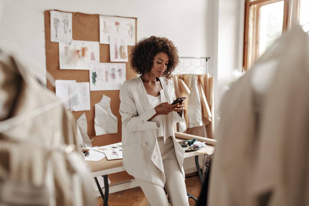 woman in a white pantsuit types on her phone