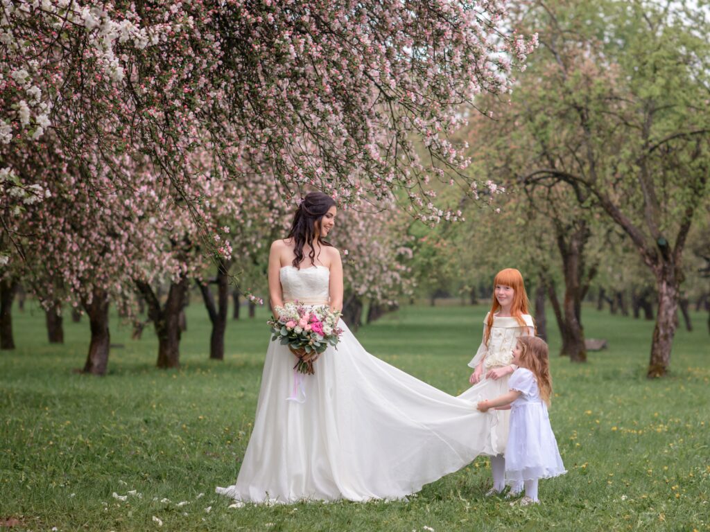 bride with two flower girls standing in orchard