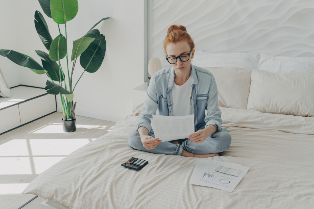 woman sitting on her bed figuring out finances