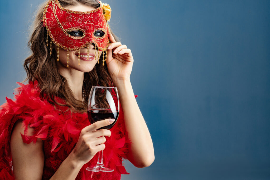 woman in a red carnival mask and boa with a raised glass of wine