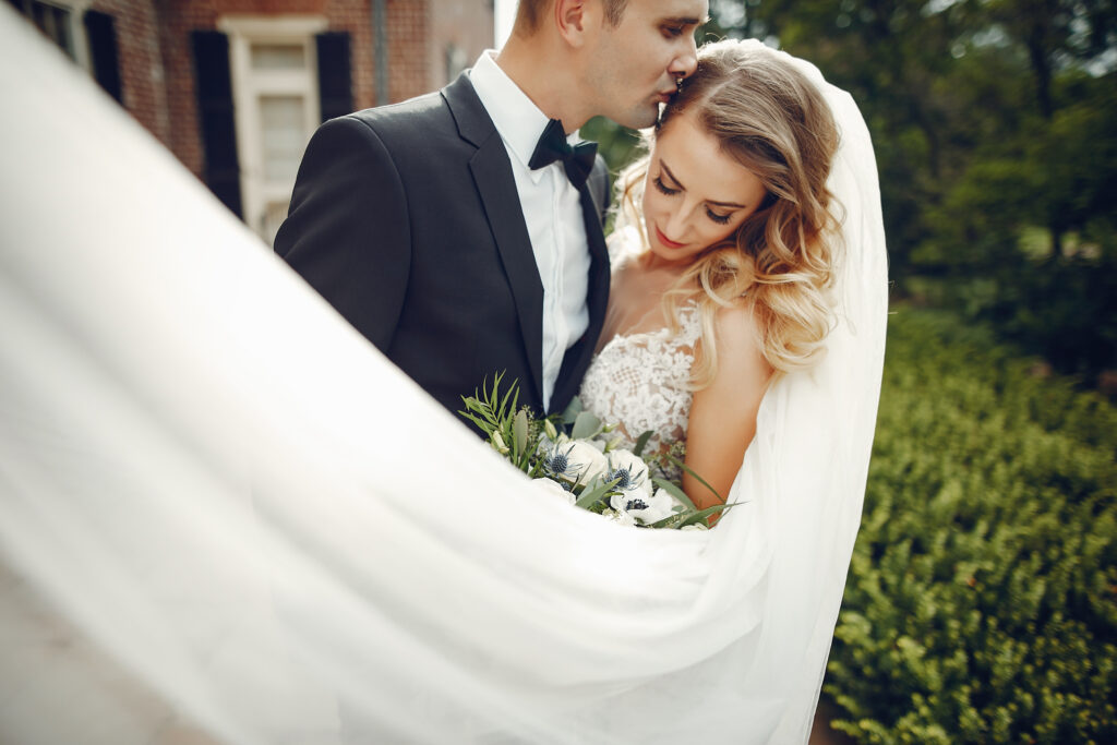 groom kisses bride as veil flows in the wind