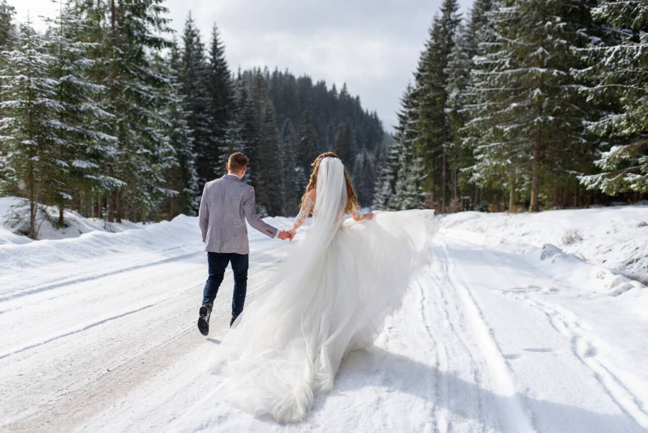 bride and groom walking down snowy path at December wedding