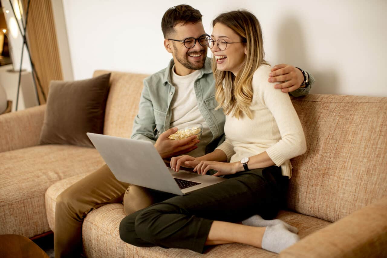 young couple sitting on couch filling out online wedding registry