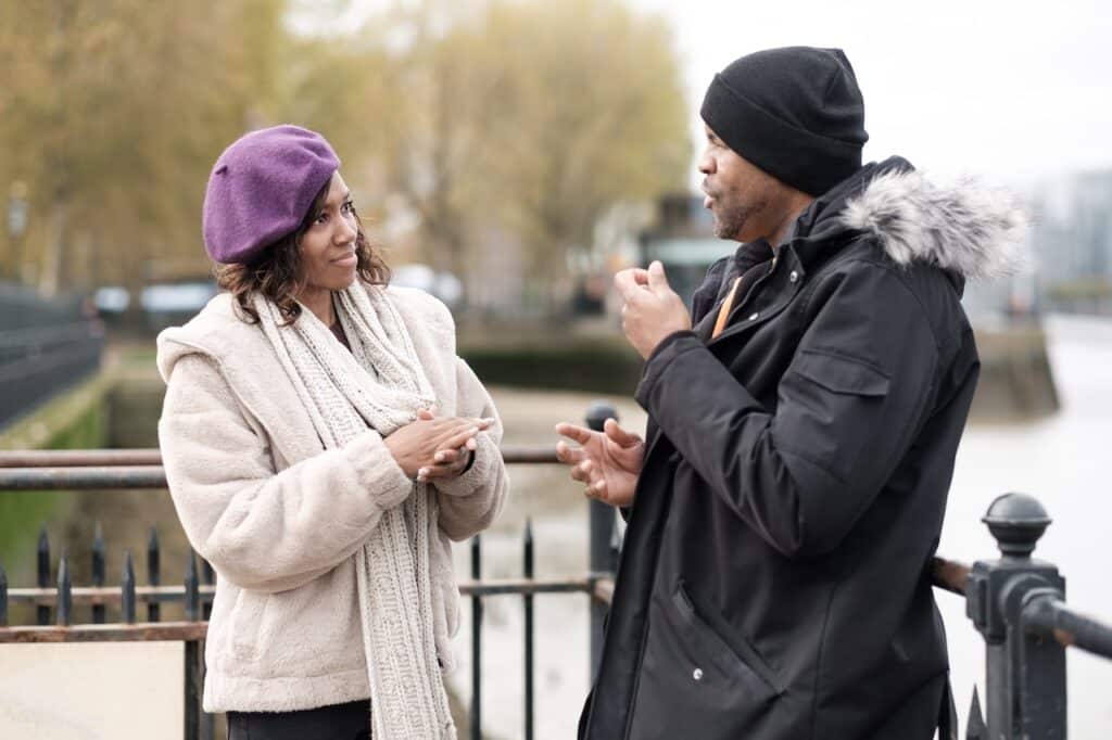 couple wearing coats standing next to river having discussion
