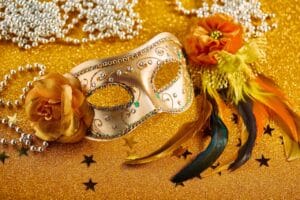 masquerade mask, feathers, and necklaces against yellow background