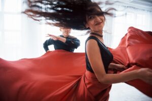 Young pretty woman in red and black clothes dancing with partner in ballroom