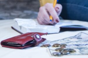 wallet, currency, and budget notebook on table with hand of person writing budget