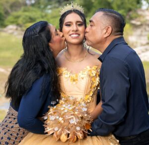 young woman with her parents who are each giving her a kiss on the cheek