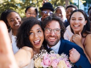 Friends, bride, and groom with wedding selfie for outdoor ceremony